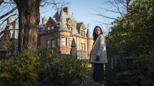 Vilket konstigt hus och vilken galen familj, tänker Marta (Ana de Armas) både en och två gånger. Marta (Ana de Armas) står vid en port och ser bakom sig. I förgrunden syns ett stort gammalt hus.