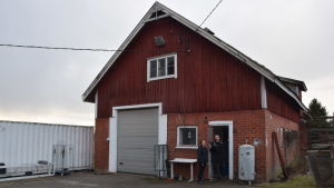 Inne i den här gamla ladugården finns ett nytt och avancerat ventilationssystem plus ganska många miljoner gräshoppor. En man och en kvinna står strax utanför en stor röd ladugård i tegel och rödmyllad brädfodring. Ute på landet, tidig vår. Ingen snö.