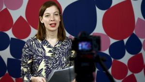 Li Andersson, Vänsterförbundets ordförande, håller förstamajtal. Li Anderson håller förstamaj-tal framför kamera med färggrann bakgrundsvägg.