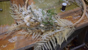 En halvfärdig krans av eterneller och torkade växter som ligger på ett bord.