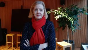 En stor del av de utmattade känner sig otillräckliga som studenter. Professor Katariina Salmela-Aro föreslår att vanlig prestation ska ses som extraordinär. Katariina Salmela-Aro med blond page och röd halsduk. Står med armarna i kors framför en växt och en vägg.