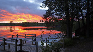 “Saunakirjassamme on paljon saunaa ja löylyjä kehuvia kommentteja”, Maarit Kirvesmäki kertoo. Saunassa on ennakkoilmoittautuminen ja saunamaksu. Järvimaisema auringon nousussa tai laskussa. Etualalla laituri ja puustoa.