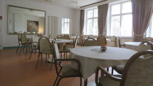 Matsalen är på samma plats, men här har kommit till en del nytt i inredningsväg. Tavlan, som du kan se via den stora spegeln, har Aki Karihtalas mamma målat. En matsal med stora fönster, stor spegel på ena väggen och flera mindre, runda bord med stolar runt borden.
