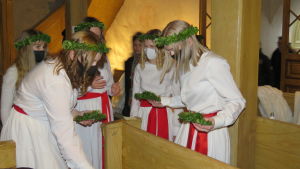 Förberedelser inför inspelning. Alla tärnor och lucia bar munskydd när kamerorna ännu var släckta. Tärnor inne i en kyrka, de har munskydd på sig. Förbereder sig, fixar bland annat med ljus och ljusmanschetter av lingonris.