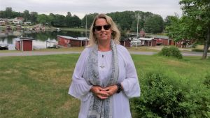 Lenita Sandell, som är född och uppvuxen i Hangö, har så att säga hittat hem igen. Fritiden tillbringas i Kapellhamnen. En kvinna med halvlångt, blont hår, solglasögon och ljusa kläder står ute med Kapellhamnen i Hangö och de små, röda fiskebodarn i bakgrunden.