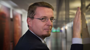 Tomi Voutilainen. Tomi Voutilainen lutar sig mot väggen med höger hand och ser bakåt, in i kameran.