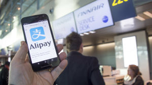 Finnair tar emot betalningar via Alipay på vissa rutter. Alipays logotyp på en telefon framför Finnairs incheckningsdesk.