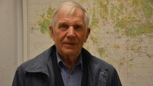 Matti Agge deltog i mötet. Äldre man med vitt hår och blå jacka står framför ett sjökort över åbolands skärgård.