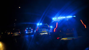 Polisbilar med blåljus kör efter varandra i mörkret.