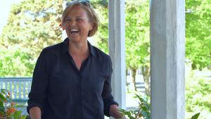 Carolina Buchert har Hangö i sitt hjärta. Carolina Buchert skrattar öppet mot kameran. Hon står på verandan vill Tellina i Hangö och planterar blommor.