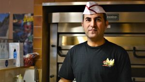 Nazar Ali driver pizzerian Kungs Pizza Kebab på Långgatan Man iklädd kockhatt står vid en pizzaugn och ser mot kameran.