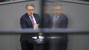 CSU-politikern Georg Nüsslein ska ha kammat in över 600 000 euro på munskyddsaffärerna och utreds nu för korruption. Den bayerske CSU-politikern Georg Nüsslein står och pratar och pekar i en talarstol. En suddig variant av honom speglas i en skärm.