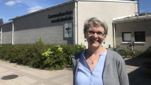 Anu Peltomäki vill att alla som gör reklam för den avgiftsfria lunchen för alla barn och familjer som går förbi. Kvinna står och ler i solen utanför Gammelbacka allaktivitetshus.