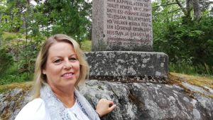 Här är minnesstenen från 1936. En kvinna med blont halvlångt hår pch ljusa kläder står vid en stor sten där det finns en minnessten.