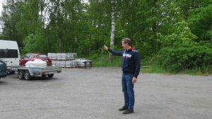Här ska det kanske byggas flervåningshus i Ingå. Robert Nyman pekar ut det nyplanerade området. En man i jeans och blå munkjacka pekar mot en skogdunge. På sandplan står några bilar parkerade.