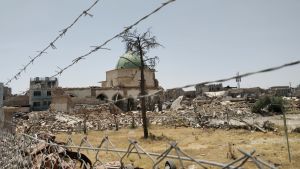 Från den numer förstörda Al-Nouri moskén utropade Islamiska staten sitt kalifat i juni 2014. Den numer förstörda Al-Nouri moskén i Mosul skymtar i bakgrunden. I förgrunden stängsel, taggtråd och bråte.