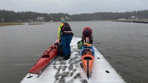 På vintern ska man aldrig paddla ensam. Charlotta och Tarja står på en snöig brygga och förbereder sina kajaker.