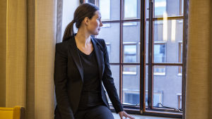 Trafikminister Sanna Marin vill inte kommentera ILMO-rapportens framtidsscenarier. Sanna Marin sitter på ett fönsterbräde och tittar ut genom fönstret.