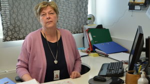 Marianne Putus är kostservicechef i Sibbo. Kvinna i ljusröd kofta sitter vid sitt skrivbord och tänker.