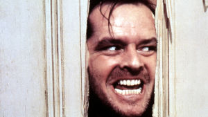 "Here's Johnny!" Jack (Jack Nicholson) blev galen på Overlook Hotel och direkt livsfarlig då han hittade en yxa. Närbild på Jack Torrance (Jack Nicholson) då han med yxa huggit ett hål i en dörr och nu med ett galet leende tittar in genom hålet.