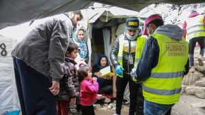 Hjälparbetare delar ut hemgjorda munskydd till flyktingar i lägret Moria på ön Lesbos. Hjälparbetare delar ut ansiktsmasker till en flyktingfamilj.