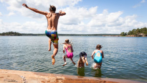 Semestertider och lättade restriktioner kan innebära att risken för smittspridning ökar. Detta kan öka trycket på vården, säger Pietilä. En kille och några barn hoppar i vattnet från en klippa.