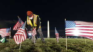 200 000 flaggor placeras ut på gräsmattan utanför Capitolium för att symbolisera publikmassan som tidigare år fått följa med presidentinstallationerna på plats. En man placerar ut små amerikanska flaggor på en gräsmatta.
