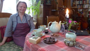 Ylva Rancken-Lutz minns hur gott det var att dricka varm choklad hos farmor. Kopparna och kannan är de samma som farmor bjöd från. En kvinna sitter vid ett bord fyllt med praliner och chokladkonfekt och kaffekoppar (Med kakaodryck)