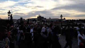 Kafka, Mozart, Havel har sett solen gå ner över Prag. Det har också miljontals turister. Delade erfarenheter svetsar oss samman som människor? Karlsbron i Prag i skymingen. Massor med människor, i bakgrunden slott