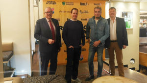 Nyckelpersonerna Ragnar Lundqvist, Petteri Ahomaa, Kalle Keskinen och Björn Siggberg. En bild på fyra män som står framför en duk som gör reklam för en festival.