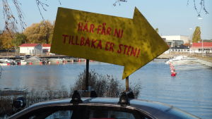 Under färden till Åland fanns en skylt på Bart Eysink Smeets tak. En skylt på ett biltak där det står "Här får ni tillbaka er sten". I bakgrunden syns en båthamn.