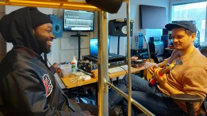 Jesse Markin och Totte Rautiainen vann en Emma för debutalbumet Folk. Jesse Markin skrattar, Totte Rautiainen spelar bas i en studio full av musikutrustning och skärmar.