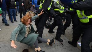 Foton och videor vittnar om att både demonstranter och poliser skadats. Kvinna drabbar samman med polis i London. Hon faller bakåt på bilden