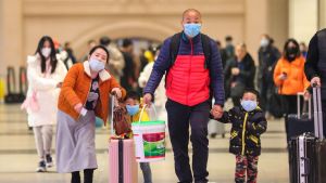 En familj bär munskydd på en tågstation i Wuhan i Kina. Risken för smitta ökar i och med att många reser iväg för att fira kinesiskt nyår. En man och en kvinna går hand i hand med två barn. De har resväskor och munskydd.