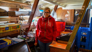 Det här blir Daniela Sandströms nionde sommar på butiksbåten. En kvinna står bakom en kassaapparat inne framför hyllor med varor.