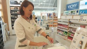 Farmaceuten Mona Rosenlund på Centralapoteket säger att folk i alla åldrar köpt munskydd. Farmaceut vid hylla för munskydd på apotek.