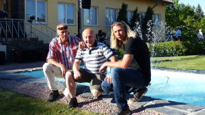 Roger Lönnberg, Karl-Johan Hellman och Henrik Lillqvist tre män sitter på huk framför en fontän. Männen är sommarklädda. Runt den lilla fontänen finns gräs och buskar.