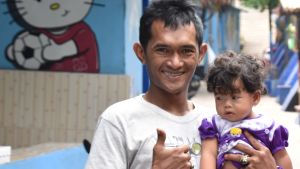 Fotbollsfantasten Imadudin Nur tar hand om sin dotter på dagarna. Samtidigt förbättrar han sin engelska genom att prata med utländska besökare. Pappa med barn i famnen i ett slumområde i Malang, Indonesien
