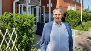 Kommundirektör Juha-Pekka Isotupa jobbar i kommunhuset trots surrande fläktar. Man framför ett hus.