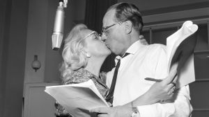 näytteljijät Ansa Ikonen ja Sasu Haapanen suukottelevat radiostudiossa käsikirjoitukset käsissään.