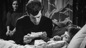 Kino klassikko: kiusaus. Mies, ilmeisesti pappi, lukee jotakin sängyssä makaavalle pojalle.