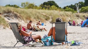 Varför vill vi vara solbrända trots att vi vet att solandet medför risker? Ett medelålders par solar i varsin solstol på en strand. I bakgrunden flera solbadare.