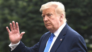 När Trump anlände tillbaka till Vita huset efter sjukhusbesöket hade han ingen mask på sig. Donald Trump klädd i kostym. Han vinkar mot kameran.