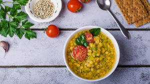 Många av de rätter man serverar i dag för vegetarianer i Lojo lämpar sig också för veganer. En sopptallrik på ett bord med en sked, två skivor knäckebröd och några tomater bredvid sig.