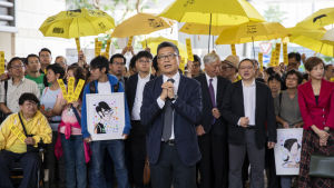 Professor Chan Kin Man som grundade ockupationsrörelsen år 2014, fick stöd av ett hundratal aktivister med gula paraplyer då han kom till domstolsbyggnaden i Hongkong Professor Chan Kin Man som grundade ockupationsrörelsen år 2014 fick stöd av ett hundratal aktivister med gula paraplyer då han kom till domstolsbyggnaden i Hongkong