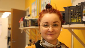 Mersiha Osmanovic. En kvinna i 30-årsåldern med rött hår och glasögon står bredvid en gul vägg i en skolkorridor.