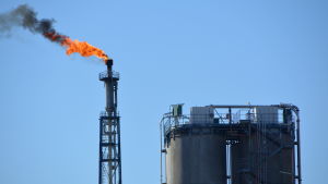 Fackling krävs vid petrokemisk industri. Arkivbild. Fackla med orange eld och svart rök, klarblå himmel.