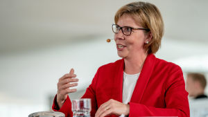 Anna-Maja Henriksson kommer från Jakobstad. Anna-Maja Henriksson står vid ett bord och pratar under regeringens presskonferens i Helsingfors centrumbibliotek Ode den 3.6.2019.