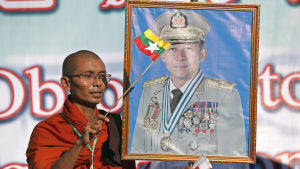 En buddhistisk munk viftade med en flagga och ett porträtt av överbefälhavare Min Aung Hlaing under en demonstration till stöd för militären i Rangoon den 14 oktober 2018. En buddhistisk munk viftade med en flagga och ett porträtt av överbefälhavare Min Aung Hlaing under en demonstration till stöd för militären i Rangoon den 14 oktober 2018.