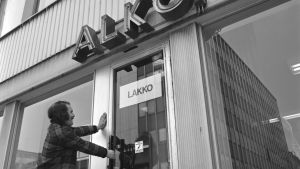 Alkon lakko 1972. Alkon lakko alkoi 24.04.1972 ja päättyi kesäkuun alussa. Alko Oy, myymälä. Ovessa lappu "Lakko". Mies yrittää avata myymälän ovea (lavastettu kuva).
